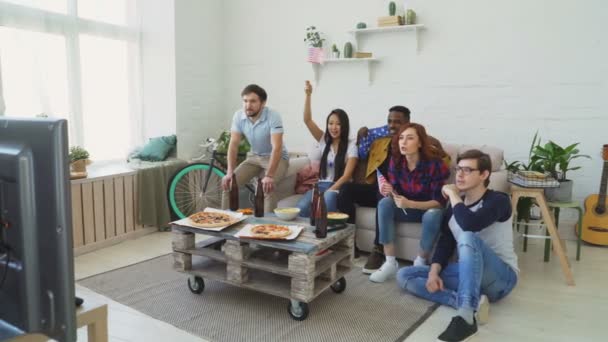 Grupo multiétnico de amigos con banderas nacionales de EE.UU. viendo el campeonato deportivo en la televisión juntos animando a su equipo favorito en casa — Vídeo de stock