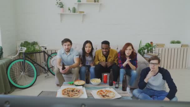 Groep jonge vrienden kijken Olympische spelen wedstrijd op Tv samen eten van snacks en drinken bier. Afrikaanse mens is blij om zijn team winnen, maar anderen zijn teleurgesteld — Stockvideo