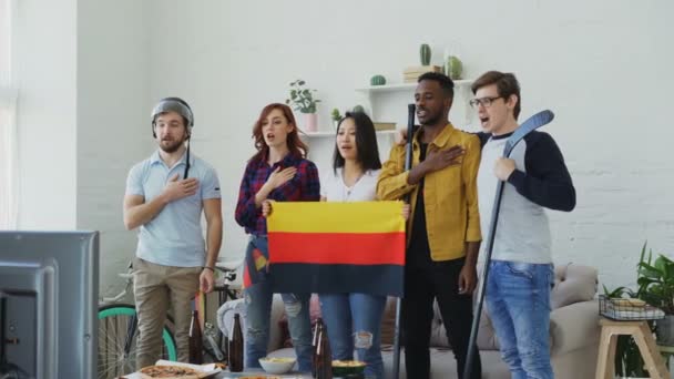 Multi ethnic group of friends listening and singing German national anthem before watching sports championship on TV together at home