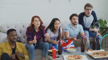 Grup genç arkadaşlar spor fanatikleri Spor şampiyonluk favori takım evde kazanan hakkında mutlu ve birlikte televizyonda izlerken İngiliz ulusal bayrakları ile