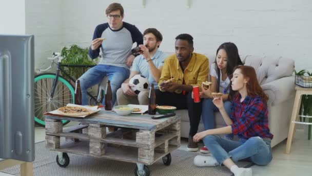 Felices amigos fanáticos de los deportes viendo el campeonato de fútbol en la televisión juntos comiendo pizza y bebiendo cerveza en casa — Vídeo de stock