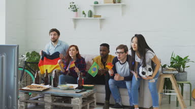 Olimpiyat Oyunları televizyonda birlikte evde maç izlerken uluslararası genç arkadaşlar. Bazıları mutlu ama Brezilyalı adam kazanan Alman ekibi hakkında hayal kırıklığına