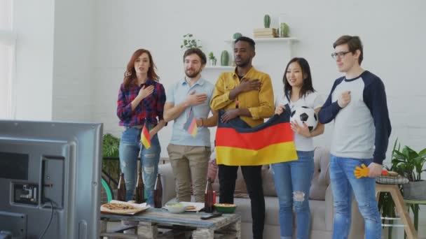 Wieloetnicznego Grupa przyjaciół, słuchania i śpiewania hymnu Niemiec przed obejrzeniem Mistrzostwa sportowego w telewizji razem w domu — Wideo stockowe