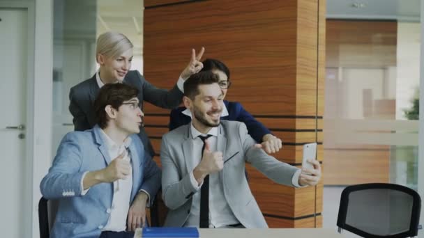 Happy business team taking selfie portrait on smartphone camera and posing for group photo during meeting in modern office — Stock Video