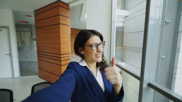 Punto de vista de la joven mujer de negocios en traje de tener chat de vídeo en línea utilizando la cámara del teléfono inteligente y hablar con sus colegas en la oficina moderna — Vídeos de Stock
