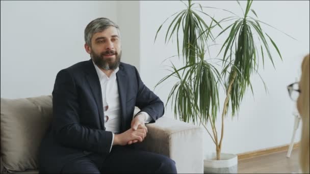 Lächelnder Geschäftsmann auf Couch im Gespräch mit seinem Psychotherapeuten im Büro — Stockvideo