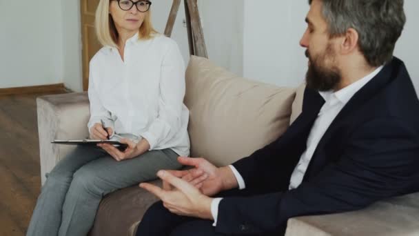 Inclinación de la mujer psiquiatra experimentada escuchando deprimida paciente hombre de negocios en su oficina — Vídeos de Stock