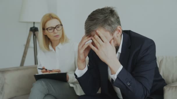Boos huilende zakenman patiënt zijn hoofd te houden door handen praten met zijn psychoanalyticus in haar kantoor — Stockvideo