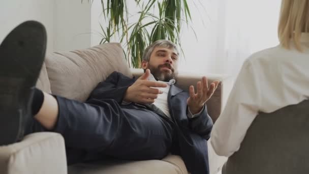 Homem deitado no sofá falando sobre seus problemas com psicoterapeuta profissional ou psicóloga em seu escritório — Vídeo de Stock