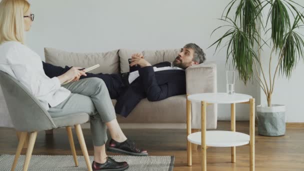 Hombre acostado en el sofá hablando de sus problemas con la psicoterapeuta profesional o psicóloga en su oficina — Vídeos de Stock