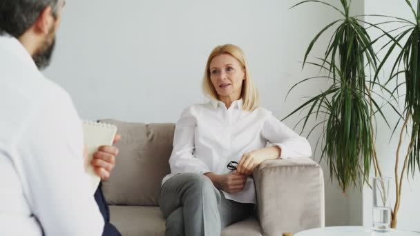 Psychanalyste homme écoute adulte femme stressée patiente et écrit des notes dans le bureau de psychologue — Video