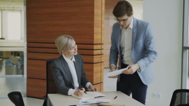 Dos colegas de negocios discutiendo informes en la oficina moderna. Mujer de negocios sentada en la mesa hablando con su pareja masculina — Vídeo de stock