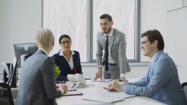 Empresaria discutiendo informes con colegas masculinos y femeninos sentados a la mesa en la oficina moderna — Vídeo de stock