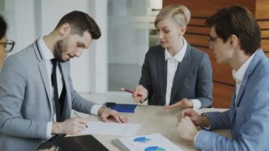 Takım elbise imzalamadaki genç işadamı sözleşme ve meslektaşı modern ofisinde oturan ortaklık ayrıntılarını açıklayan şirket avukatı süre ile el sallamak