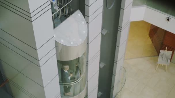 Наклон деловых женщин и коллег бизнесменов, говорящих в движущемся лифте и выходящих из него в современном бизнес-центре — стоковое видео