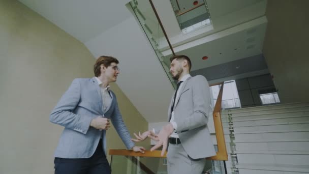 在现代商务中心大厅的两位商人同事站在栏杆旁站着聊天 — 图库视频影像
