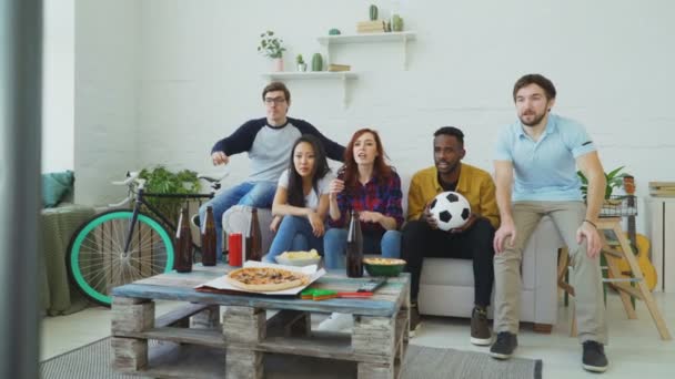 Multi gruppo etnico di amici appassionati di sport guardando partita sportiva in TV insieme mangiare spuntini e bere birra a casa — Video Stock