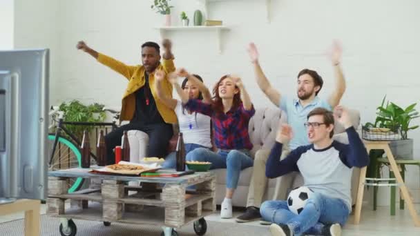 Grupo de amigos felizes assistindo jogo de esportes na TV em casa. Eles animando a equipe favorita e batendo palmas — Vídeo de Stock