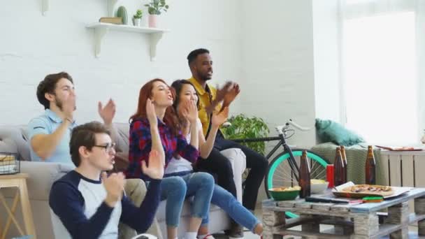 Amigos felizes fãs do esporte assistindo jogo de esportes na TV em casa. Eles animando a equipe favorita e batendo palmas — Vídeo de Stock