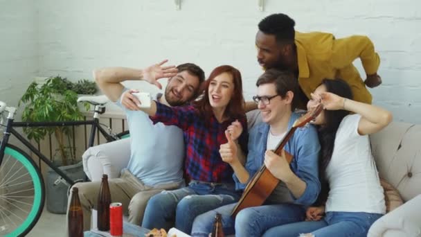 Felices amigos estudiantes tomando selfie en la cámara del teléfono inteligente y posando mientras tienen fiesta en casa en un alojamiento compartido en interiores — Vídeos de Stock