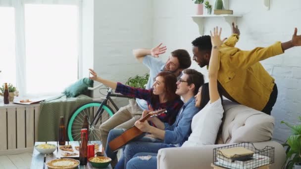 Grupa etniczna Multi Wesołych przyjaciół biorąc selfie zdjęcia na smartfonie aparatu podczas obchodzi party piwo i przekąski w domu pomieszczeniu — Wideo stockowe