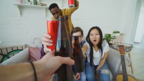 Punto de vista de toma de mano masculina tintineo botella de cerveza con amigos mientras se celebra la fiesta en casa en el interior — Vídeos de Stock