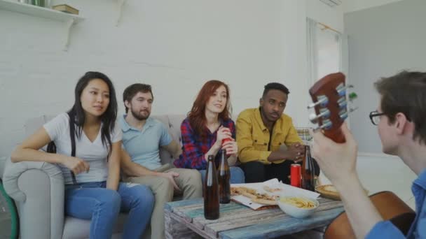 Fröhliche junge Freunde feiern zu Hause zusammen Gitarre spielen und singen — Stockvideo