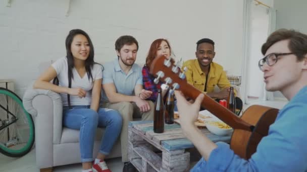 Щасливі молоді друзі влаштовують вечірку, граючи на гітарі та співаючи разом вдома — стокове відео