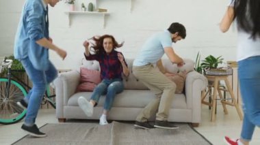 Yavaş çalışan ve kanepeye atlama sonra gülümseyerek ve gösterilen genç arkadaşlar evde hep birlikte Yaşasın