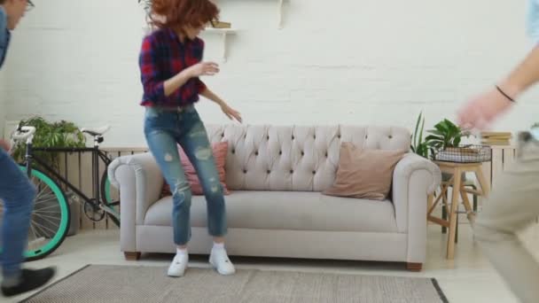 Slow motion av unga vänner kör och hoppa på soffa sedan ler och tittar in kameran alla tillsammans hemma — Stockvideo