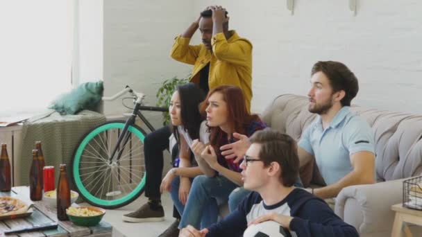 Cámara lenta de amigos jóvenes viendo el partido de fútbol en la televisión juntos en casa y decepcionados por su equipo favorito perder el partido — Vídeos de Stock