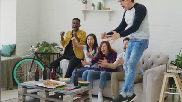 Mouvement lent de jeunes amis heureux regardant le jeu de sport à la télévision sauter et célébrer la victoire de l'équipe préférée à la maison — Video