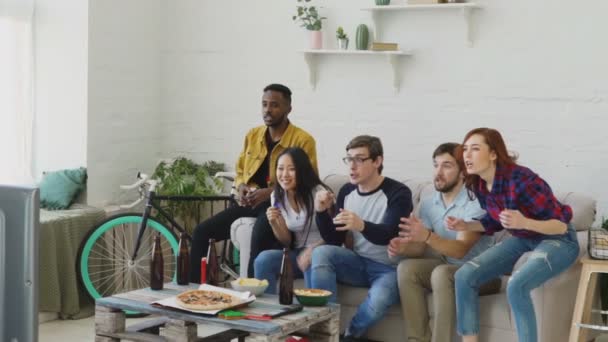 Movimiento lento de grupo multiétnico de amigos fanáticos de los deportes viendo el partido deportivo en la televisión juntos saltando y animando a un nuevo objetivo en casa — Vídeos de Stock