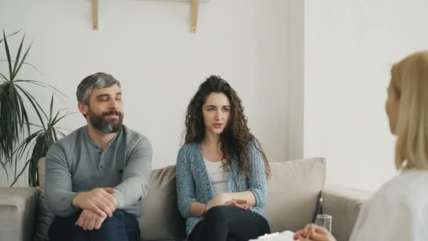 Pareja sonriente escuchando y hablando con psicólogo profesional y resolviendo porblemas de relación durante la visita al consultorio de psicoterapeutas — Vídeos de Stock