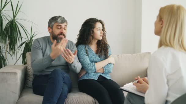 Hombre enojado discutiendo y hablando de su esposa con el consejero matrimonial. Pareja joven visitando consultorio psicólogo profesional — Vídeos de Stock