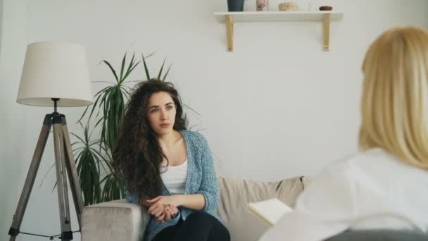 Lächelnde Frau, die auf dem Sofa sitzt und nervös mit einer Psychoanalytikerin spricht und im Büro des Psychotherapeuten Hände gestikuliert — Stockvideo