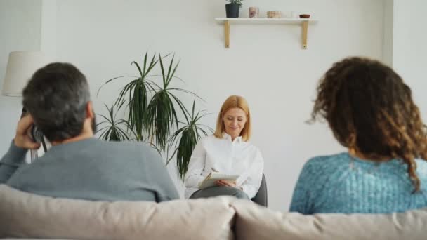 Női szakmai pszichológus hallgató és írás megjegyzi, notebook, míg a fiatal nő barátja beszélt telefonon során látogatást pszichoterápia office beltéri vitatkozni — Stock videók
