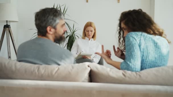 Psychanalyste expérimentée féminine écoutant et écrivant des notes tandis que le couple marié en colère se disputant et se querellant pendant la visite psychologue professionnel et bureau de conseiller de mariage — Video