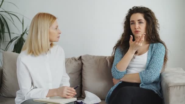 Upset crying girl having consultation with professional female psychologist who giving paper tissue to stressed woman in psychotherapist office indoors — Stock Video