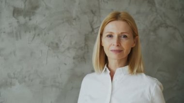Gülümseyen ve kameraya gri arka plan üzerinde seyir çekici orta yaşlı bir kadın portresi yakın çekim