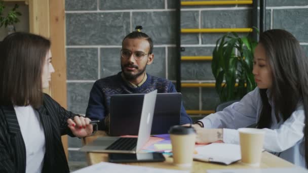 Grupo de personas multiétnicas sentadas en el escritorio con ordenadores portátiles trabajando y hablando de un nuevo proyecto de puesta en marcha en la moderna oficina loft — Vídeos de Stock