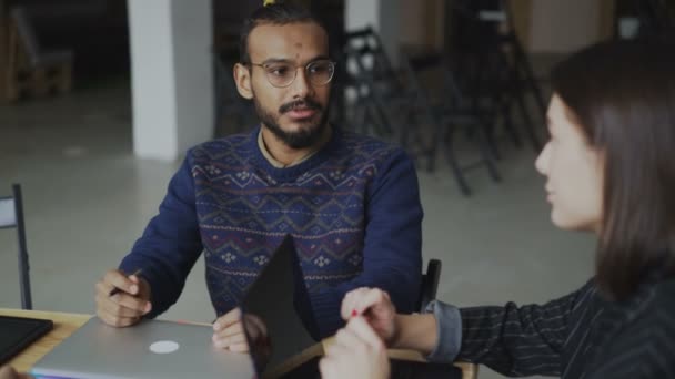 Joyeux homme afro-américain en lunettes souriant et discutant d'un nouveau projet de start-up avec une collègue féminine dans un bureau loft à l'intérieur — Video