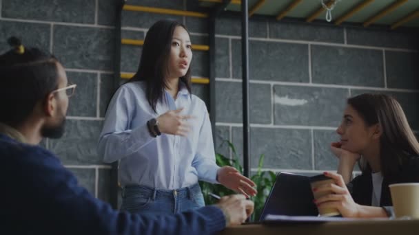 容アジアの女性の話と、近代的なオフィス室内にスタートアップ プロジェクトのブレーンストーミング中に創造的なチームで、新しいアイデアを議論します。 — ストック動画