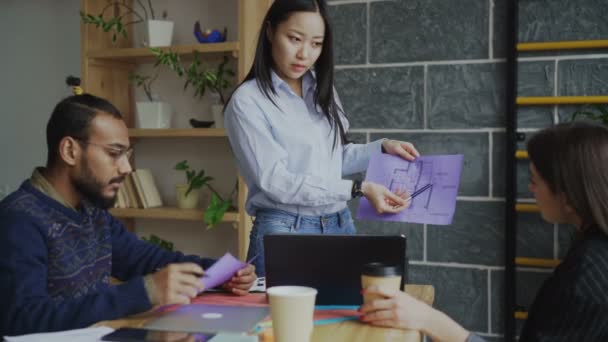 Joven mujer asiática presentando papel plan arquitectónico de casa a equipo multiétnico en moderna oficina de puesta en marcha — Vídeo de stock