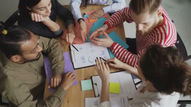 Visão superior da equipe jovem de colegas de negócios masculinos e femininos assistindo e discutindo novos gráficos de projetos de start-up no escritório loft moderno — Vídeo de Stock