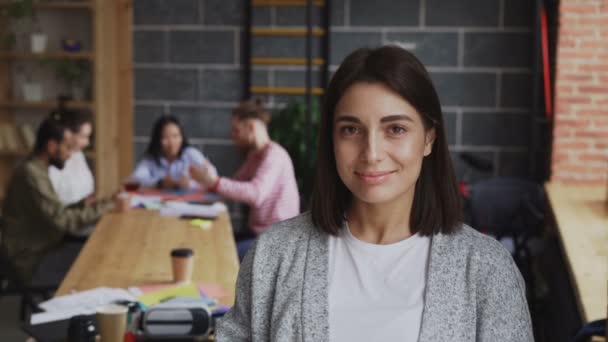 Portrait of young cheerful female entrepreneur looking at camera and smiling on busy start-up office background
