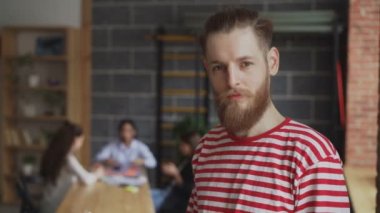 Gülümseyen ve kamera modern loft ofiste çalışan meslektaşları süre bakarak genç hipster işadamı portresi