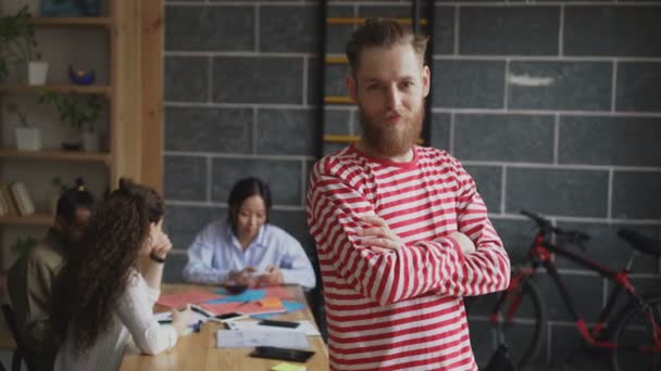 Portrait de jeune entrepreneur masculin hipster souriant et regardant la caméra tandis que ses collègues travaillant au bureau loft moderne — Video