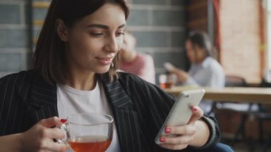 Kadın girişimci sörf smarpthone gülümseyerek ve sahip meşgul ofiste kırmak ise çay içme