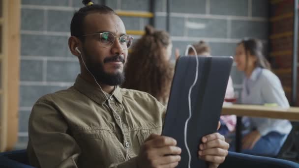 Africano americano homem em óculos segurando smartphone e ter videochamada on-line, enquanto seus colegas trabalhando no escritório moderno — Vídeo de Stock